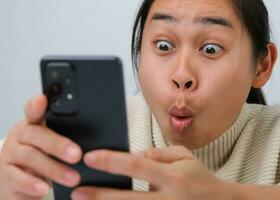 Portrait of happy woman enjoying success on mobile phone at home. Close-up of happy young woman reading good news on the phone. Surprised woman celebrating success on the phone. photo