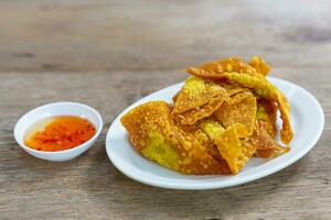 Delicious Thai style crispy homemade fried pork dumplings in white ceramic plate with dipping sauce in ceramic cup delicious Thai appetizers on wooden table. photo