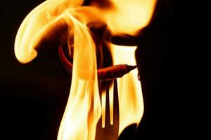 Chili pepper on fork with flames on black background. Burning red chili pepper. Slow motion photo