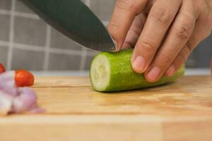 Female hand using a knife to slice cucumbers on a cutting board. Close-up. Woman with kitchen knife cutting cucumber at home. Preparing homemade food photo