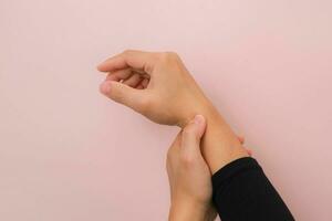 Close-up of woman's hand holding her painful wrist from Arthritis or Carpal Tunnel Syndrome CST isolated on pink background. Health care concept. photo