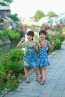 Two cute little sisters smiling and looking at the camera along the Khlong Mae Kha. A waterfront village that has recently been transformed into a new night market in Chiang Mai, Thailand. photo