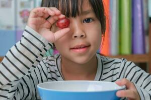 Little girl eating fresh red grapes at home in the living room. Cute young Asian girl eats healthy fruits and milk for her meal. Healthy food in childhood photo