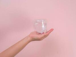 Female hand holding glass of water isolated on pink background. photo