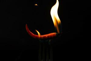 Chili pepper on fork with flames on black background. Burning red chili pepper. Slow motion photo