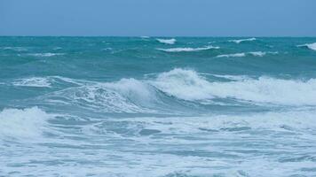 View of sea waves on the beach of tropical seas in Thailand. Strong sea waves crash to shore in the rainy season. Beautiful sea waves with foam of blue and turquoise color. photo