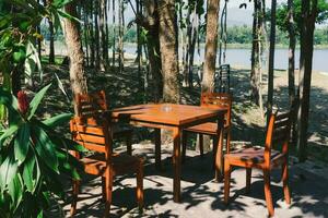 de madera mesas y sillas en un hermosa verde jardín. mueble conjunto de mesas y sillas para al aire libre viviendo. foto