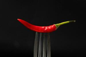 rojo chile pimienta en un tenedor en negro antecedentes. picante comida concepto. foto
