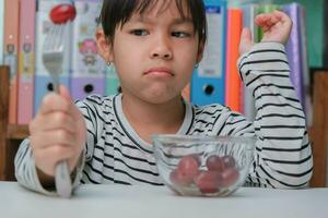 Children don't like to eat fruits. Cute young Asian girl refusing to eat healthy fruits. Nutrition and healthy eating habits for children. photo