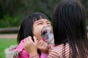 Two happy sisters exploring nature with magnifying glass outdoors. Child playing in the forest with magnifying glass. Education and discovery concept. photo