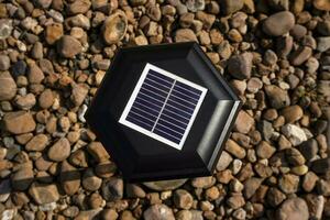 Small solar garden lights in the park. Solar powered lamp on pebbles background. Top view, selective focus on small solar panels on the lantern. photo