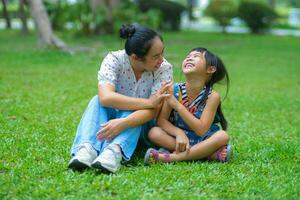 madre y pequeño hija sentado en el césped juntos en el parque. madre teniendo divertido con su pequeño hija al aire libre en verde naturaleza parque. contento familia concepto. de la madre día foto