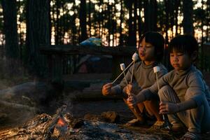 lindas hermanitas asando malvaviscos en una fogata. niños divirtiéndose en el fuego del campamento. acampar con niños en el bosque de pinos de invierno. familia feliz de vacaciones en la naturaleza. foto