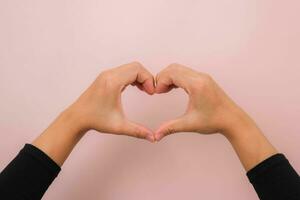 Female hands making heart symbol isolated on pink background with copy space. Love concept on Valentine Day. photo