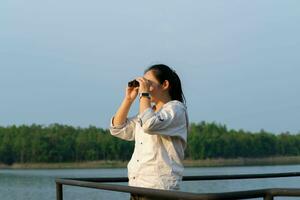 joven hembra explorador con prismáticos explorador naturaleza o acecho aves al aire libre. joven mujer mirando mediante prismáticos a aves en el reservorio. ornitología foto