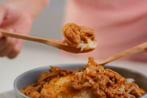 coreano comida - manos participación un cuchara comiendo salteado kimchi y kurobuta Cerdo con al vapor arroz en un bol. coreano hecho en casa comida para almuerzo foto