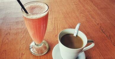 Hot coffee in a white coffee cup and a guava juice is placed on a wooden table in a warm and light atmosphere photo