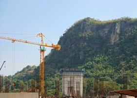 A yellow huge tower crane behind a green forest against a mountain. Construction and development of cities. photo