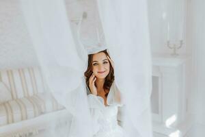 beautiful and gentle girl bride with long brown hair under a veil looks into the camera lens photo