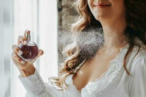 a girl in a white open dress holds purple perfume in her hands and sprays it on herself. Close-up photo