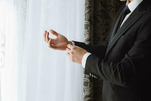 young man fastens his jacket in his hands in his room, near the window in the hotel room, young businessman, close-up photo. The groom is preparing for the wedding ceremony photo