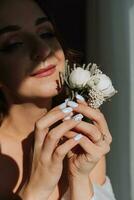 the groom's boutonniere is arranged from rose flowers in the hands of the bride with a French manicure in the wonderful natural light from the window photo