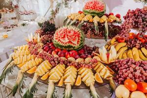 table with various fruit decorations. Watermelon carving, pineapple slices, grapes, orange photo