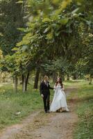 el novia y novio sostener manos, caminar en el jardín mirando a cada otro foto