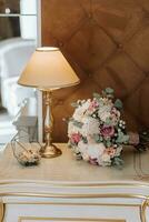 wedding details photographed from the side against the background of a night lamp, bridal bouquet, wedding rings in a glass box decorated with flowers photo