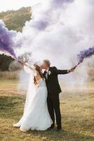 bride and groom playing with colored smoke in purple hands, hugs and kisses. Smoke bombs at a wedding. photo