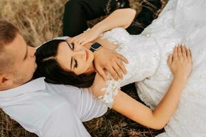 el novia y novio son acostado en el seco césped y abrazando, un mujer en un blanco Boda vestido. hermosa otoño Boda foto. foto