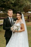 retrato de el novia y novio en el parque, el novia y novio Mira dentro el cámara lente. Boda caminar en el parque foto