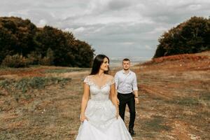 el Boda Pareja es caminando en el montañas en el antecedentes de el otoño bosque, el novia es en el primer plano foto
