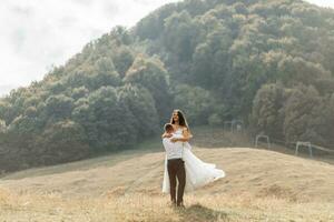 Wedding couple, walks in the mountains. Photo of a wide plan. Free space. The groom spins the bride in his arms, the bride's dress develops in the wind.