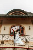 retrato de el novia y novio en contra el antecedentes de el ventana de un antiguo auténtico casa, abrazos y besos. gratis espacio. Boda caminar en el parque foto