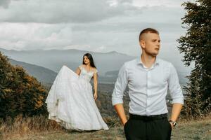 Beautiful bride and groom on the background of autumn mountains in front. A luxurious white dress flutters. The bride is in the background. Wedding ceremony on top of the mountain. Free space. photo