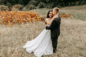 Romantic fairytale couple of newlyweds hugging and kissing in a field at sunset and ferns photo