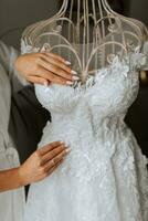 retrato de el novia con estudio ligero en su habitación. un niña en un blanco túnica demuestra su Boda vestir en un maniquí. manos cerca arriba foto