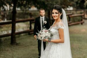 Portrait of a brunette bride in a white wedding dress with a wedding bouquet in the park. Full length photo. White lace wedding dress photo