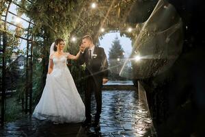 el novia y novio son caminando en el noche parque con un ramo de flores de flores y verdor, verdor en naturaleza. romántico Pareja de recién casados al aire libre. Boda ceremonia en el botánico jardín. foto