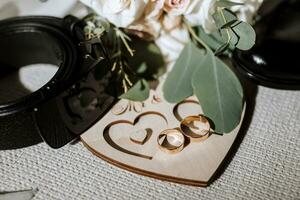 details of the groom are arranged in a composition. Black shoes, wedding bouquet, gold wedding rings on a wooden stand, black men's belt photo