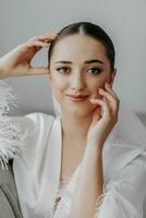 Portrait of a beautiful bride girl with stylish hairstyle and makeup in a white robe posing looking into the lens photo