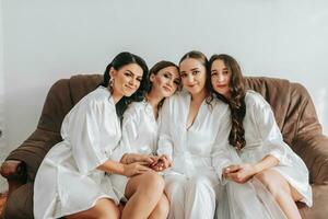 The bridesmaids are looking at the camera together with the bride. The bride and her fun friends are celebrating a bachelorette party in matching dresses. Bride and friends in the room photo