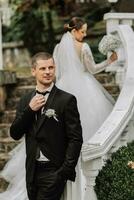 Portrait of the bride and groom on the steps in the garden, the groom in the foreground touching his tie photo