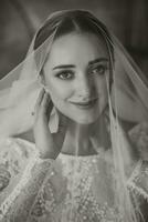 artistic portrait of a beautiful bride with wedding hairstyle and makeup under a veil. He looks into the lens and gently touches his face with his fingers. Black and white photo