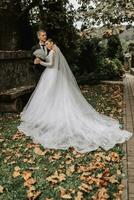 Classic full-length portrait of the bride and groom in the park among greenery and oak leaves, elegant dress with a long train photo