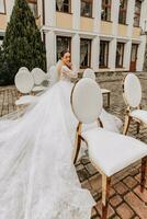 A bride with a long train sits on white chairs with gold edges after the wedding ceremony photo