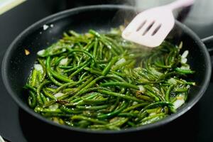 cooking greens, asparagus, garlic bunches, on a black pan and an electric stove, close-up photo