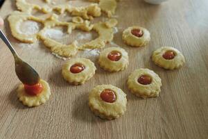 In the kitchen. A woman prepares homemade cookies with apple jam. Pieces of dough are kneaded on a wooden board, on which you need to spread apple jam. Homemade baking remains popular. photo