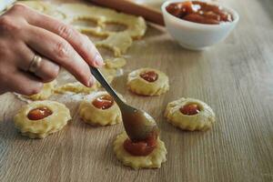 In the kitchen. A woman prepares homemade cookies with apple jam. Pieces of dough are kneaded on a wooden board, on which you need to spread apple jam. Homemade baking remains popular. photo